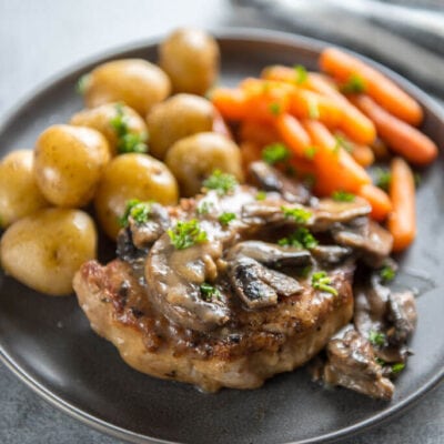 Instant Pot Pork Chops with Mushroom Gravy on round gray plate with whole baby potatoes and carrots