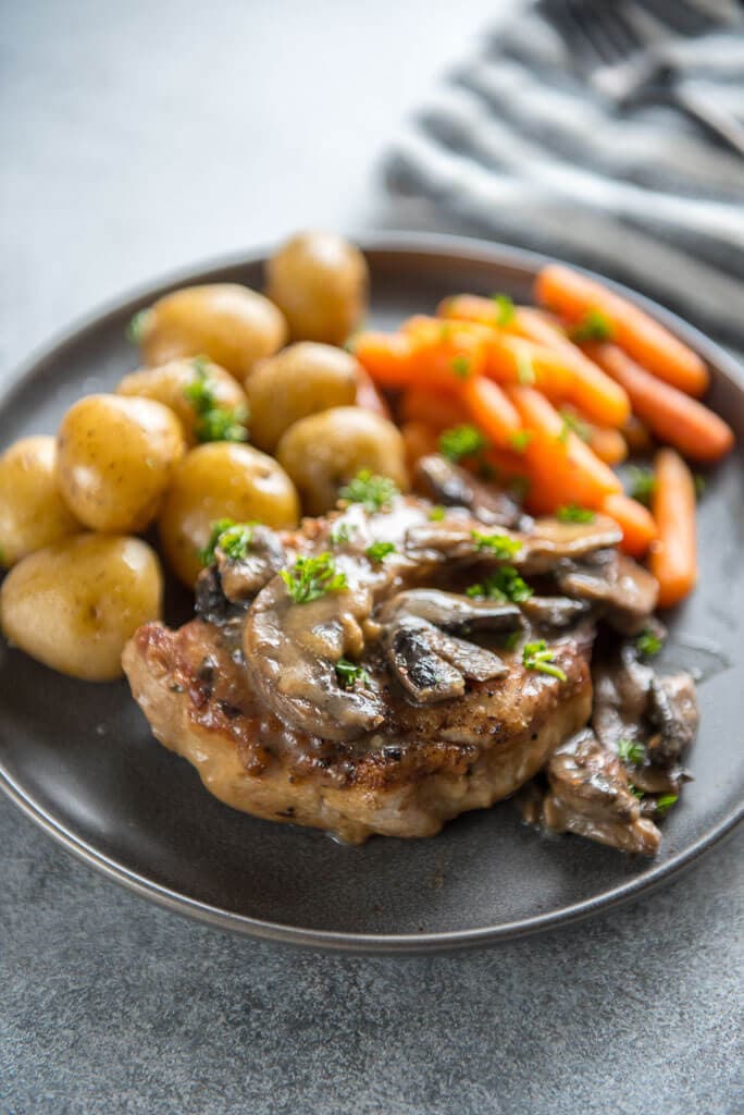 Instant Pot Pork Chops with Mushroom Gravy on round gray plate with whole baby potatoes and carrots