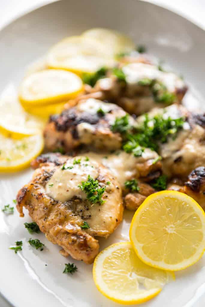 Slow Cooker Chicken Thighs with Creamy Lemon Sauce on white platter with sliced lemons