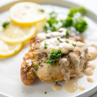 Slow Cooker Chicken Thighs with Creamy Lemon Sauce on white plate with sliced lemons