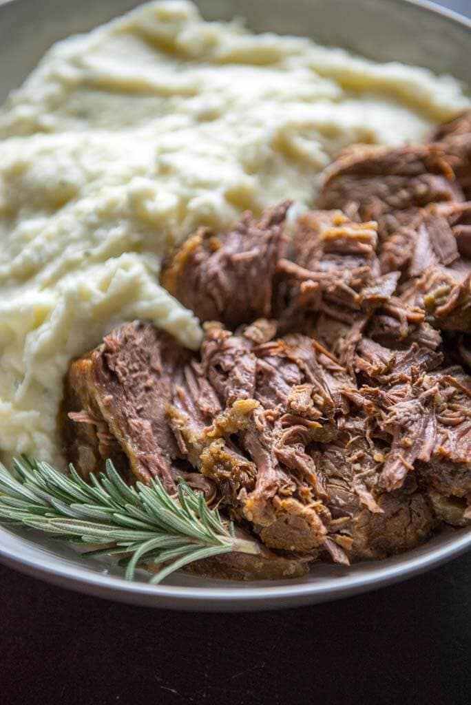 Slow Cooker Roast Beef with mashed potatoes in a white bowl with a sprig of rosemary