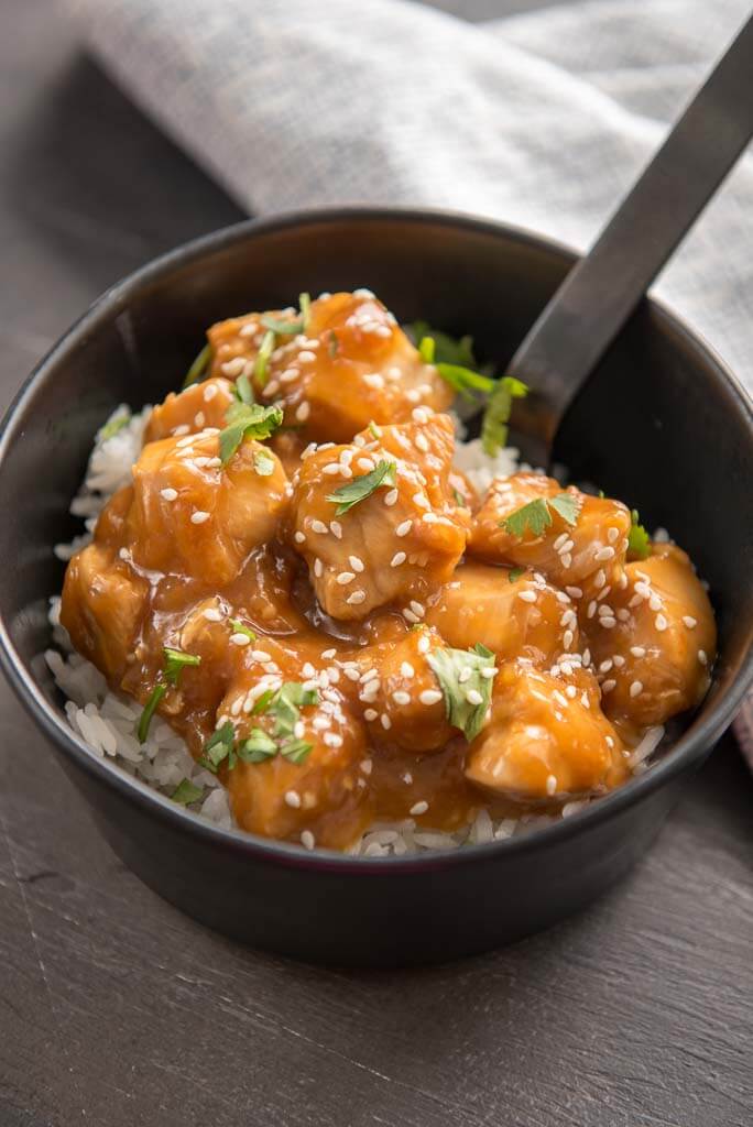 sesame chicken over rice in black bowl