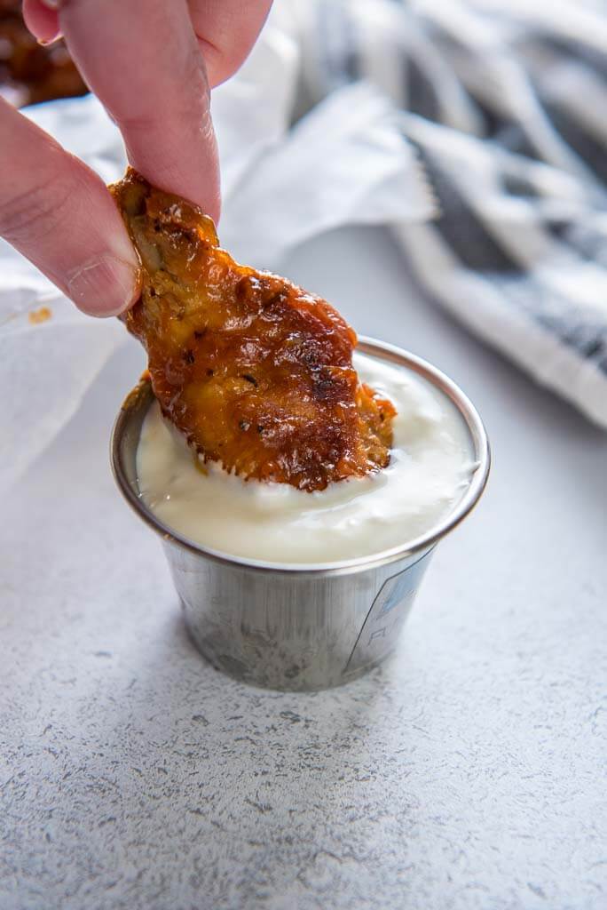 chicken wing being dipped into ramekin of blue cheese dressing