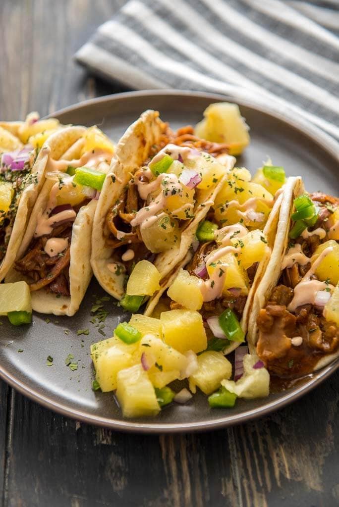 slow cooker asian pulled pork tacos topped with with pineapple salsa on gray plate