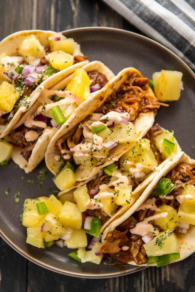 slow cooker asian pork tacos in flour shells topped with pineapple salsa on a gray plate