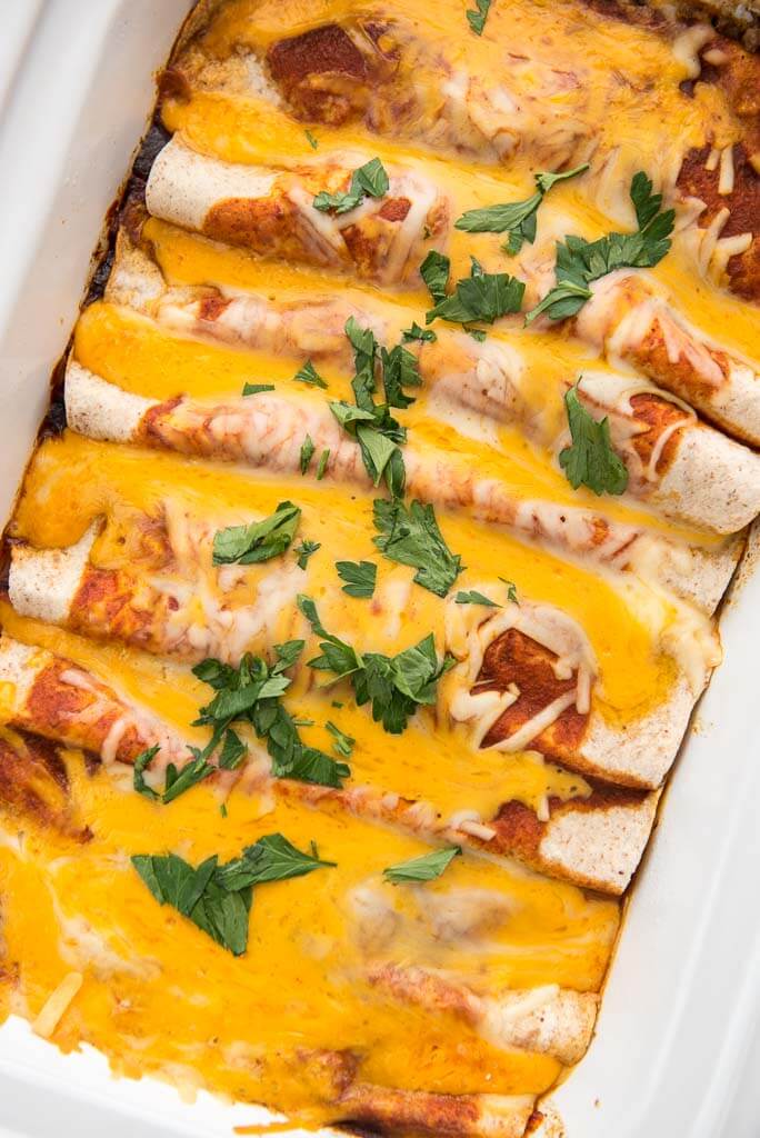 slow cooker enchiladas topped with melted cheese in casserole slow cooker