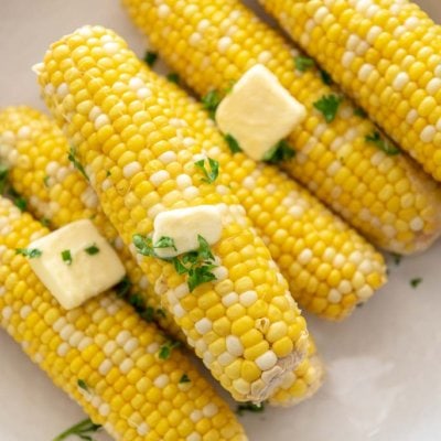 6 ears of corn on the cob in a white bowl topped with butter and cilantro