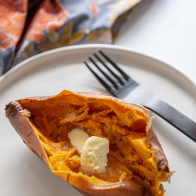 Instant Pot Sweet Potato cut open with butter on top on white plate
