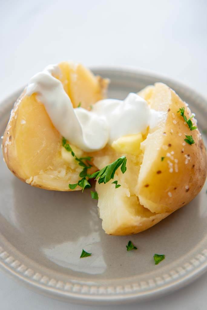 slow cooker baked potato on gray plate cut open topped with butter and sour cream