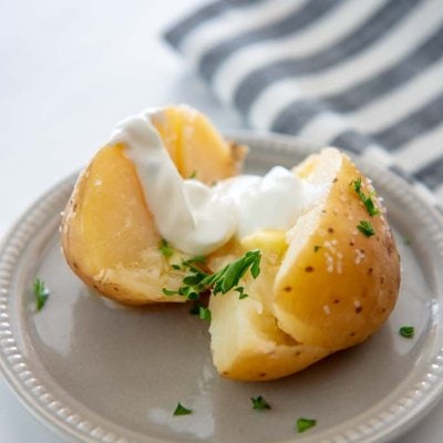 slow cooker baked potato on gray plate cut open topped with butter and sour cream
