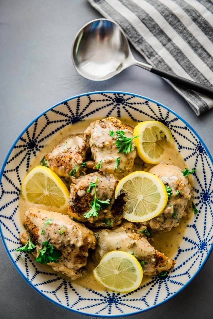 chicken thighs in a blue and white serving bowl topped with lemon slices