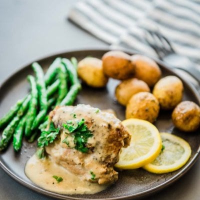 chicken thighs with lemon sauce, lemon slices, green beans and baby potatoes on a gray plate