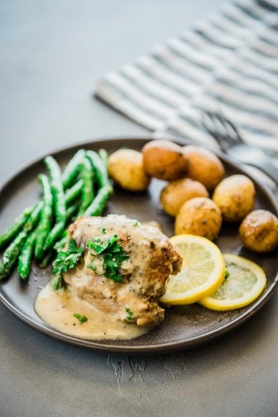 chicken thighs with lemon sauce, lemon slices, green beans and baby potatoes on a gray plate