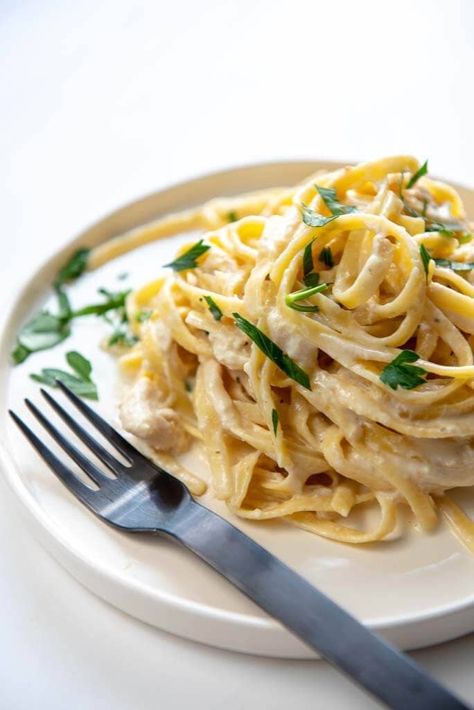 slow cooker chicken Alfredo Pasta twirled on a white plate with a black fork