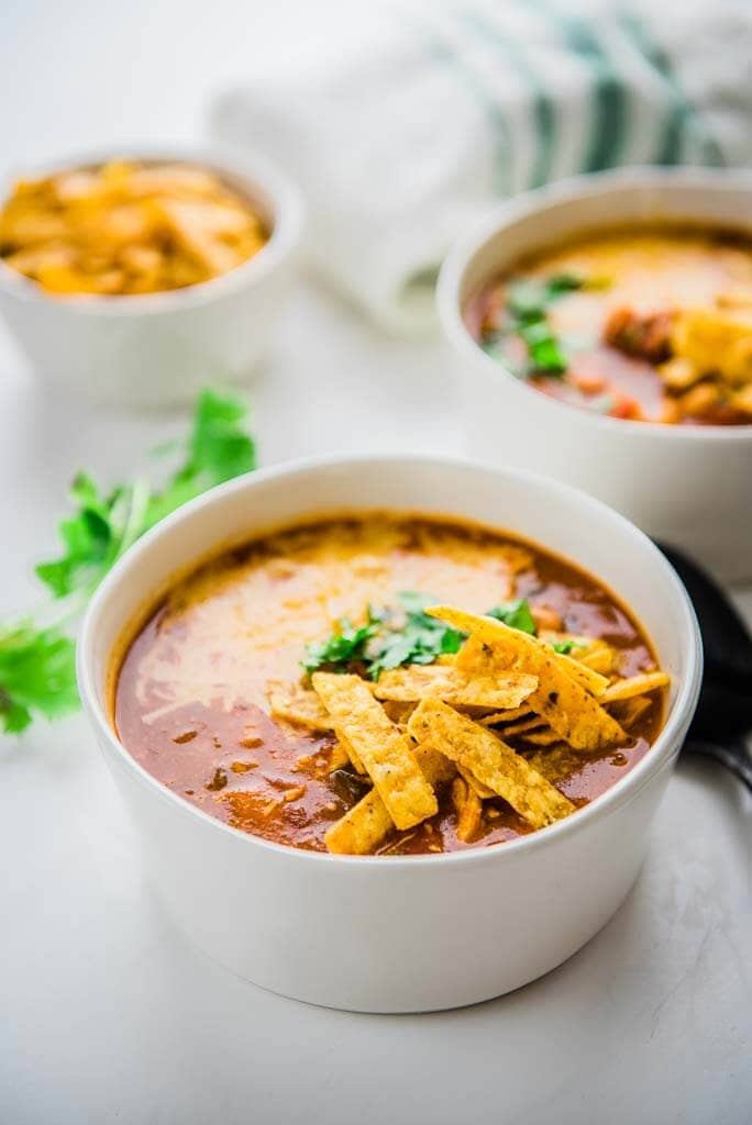 slow cooker spicy chicken enchilada soup in white bowls topped with tortilla strips and cilantro