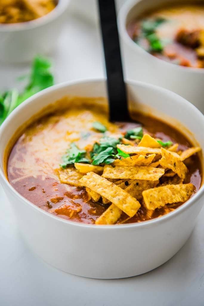 slow cooker spicy chicken enchilada soup in white bowls topped with tortilla strips and cilantro