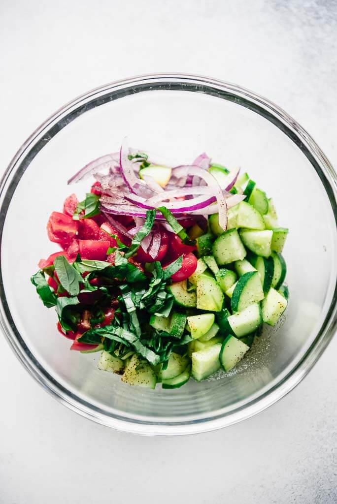 glass bowl filled with chopped cucumbers tomatoes onions and basil