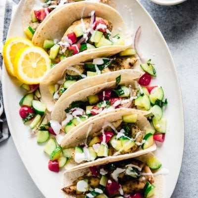 greek chicken tacos topped with cucumber tomato salsa on a white oval platter