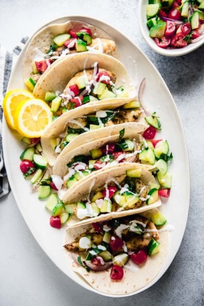 greek chicken tacos topped with cucumber tomato salsa on a white oval platter