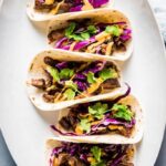 Korean beef tacos on a white platter topped with red cabbage and Sriracha mayo
