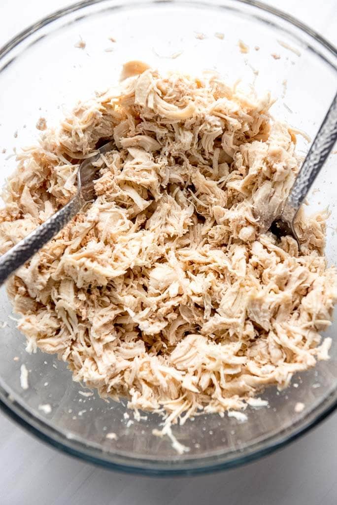 shredded chicken with two forks in glass bowl