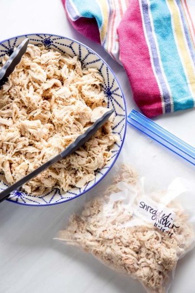 shredded chicken in a blue and white bowl next to freezer bag with shredded chicken and striped towel