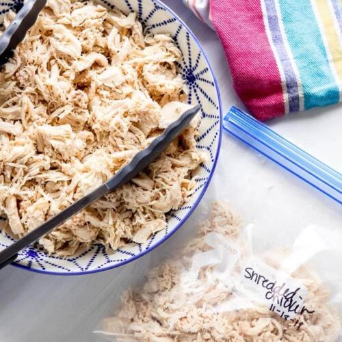 shredded chicken in a blue and white bowl next to freezer bag with shredded chicken and striped towel