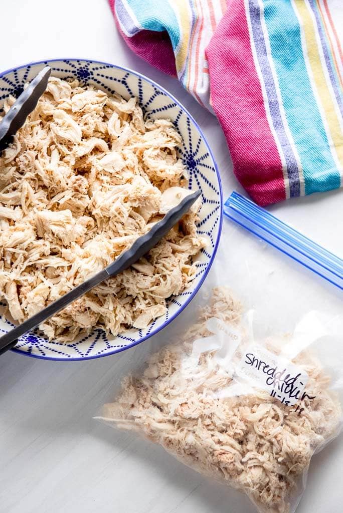 shredded chicken in a blue and white bowl next to freezer bag with shredded chicken and striped towel