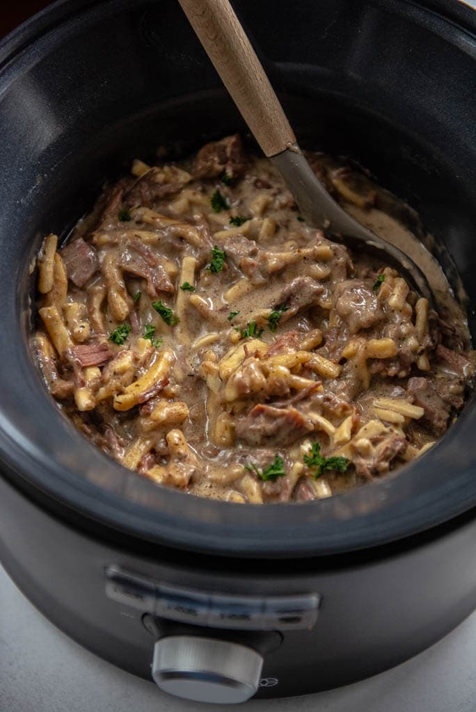 beef and noodles in a slow cooker with a serving spoon
