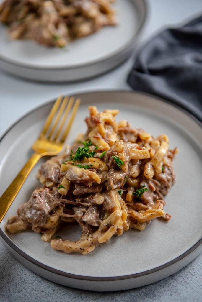 beef and noodles on a white plate with a gold fork