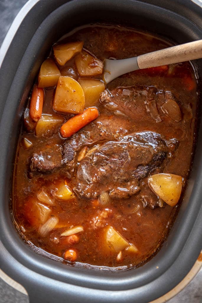 looking down into slow cooker full of pot roast, carrots, potatoes and gravy