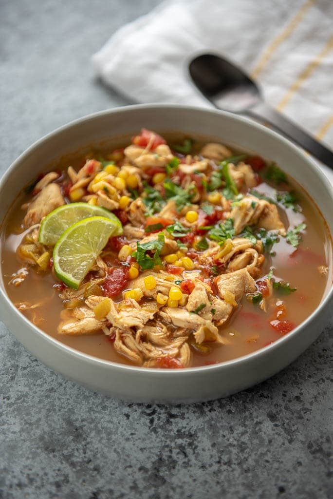 gray bowl of slow cooker spicy chicken soup topped with limes