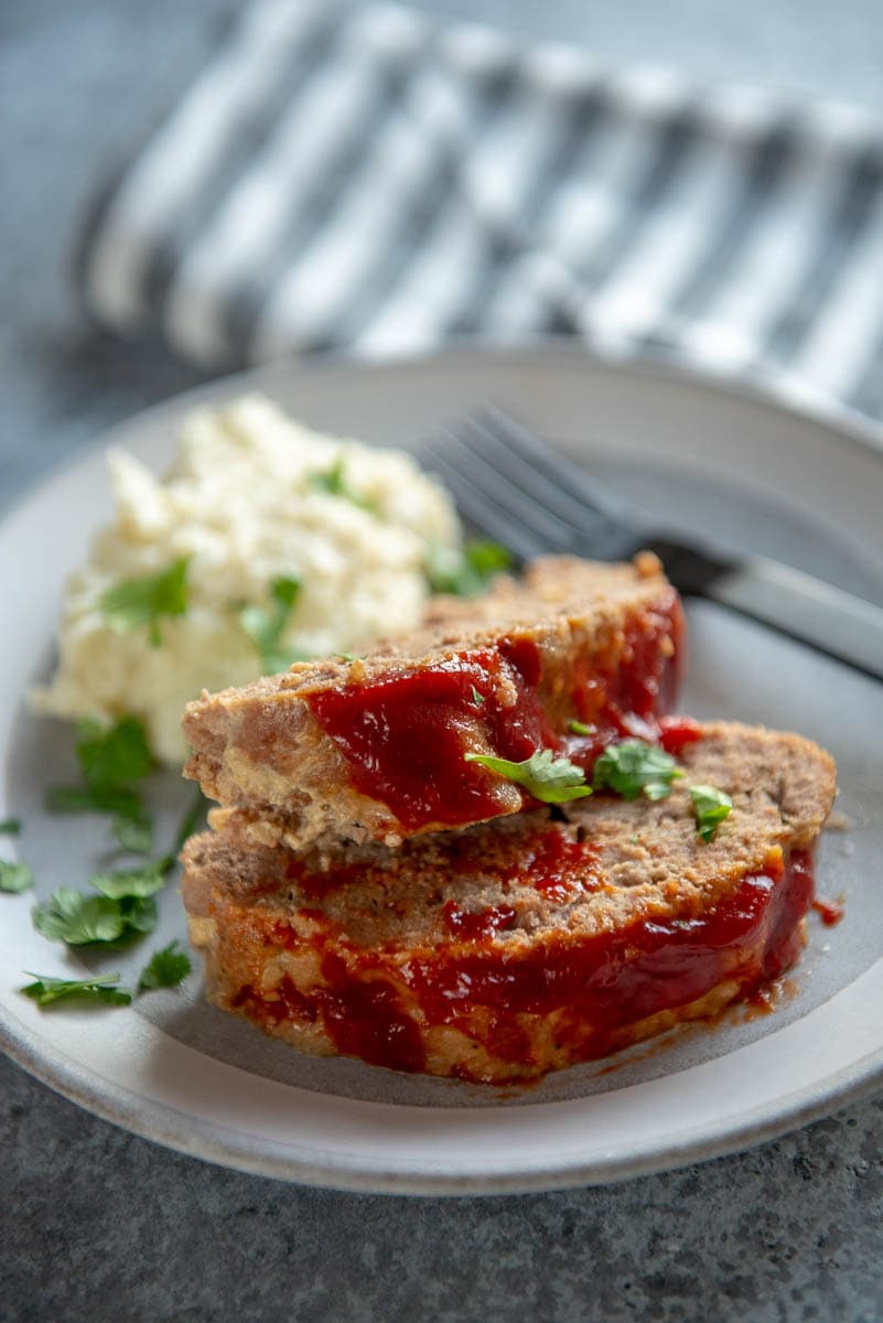 2 slices of turkey meatloaf on a gray plate with mashed cauliflower