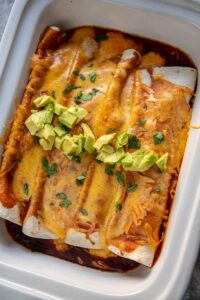 butternut squash enchiladas topped with avocado in a casserole slow cooker