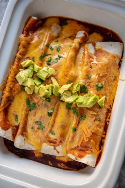 butternut squash enchiladas topped with avocado in a casserole slow cooker
