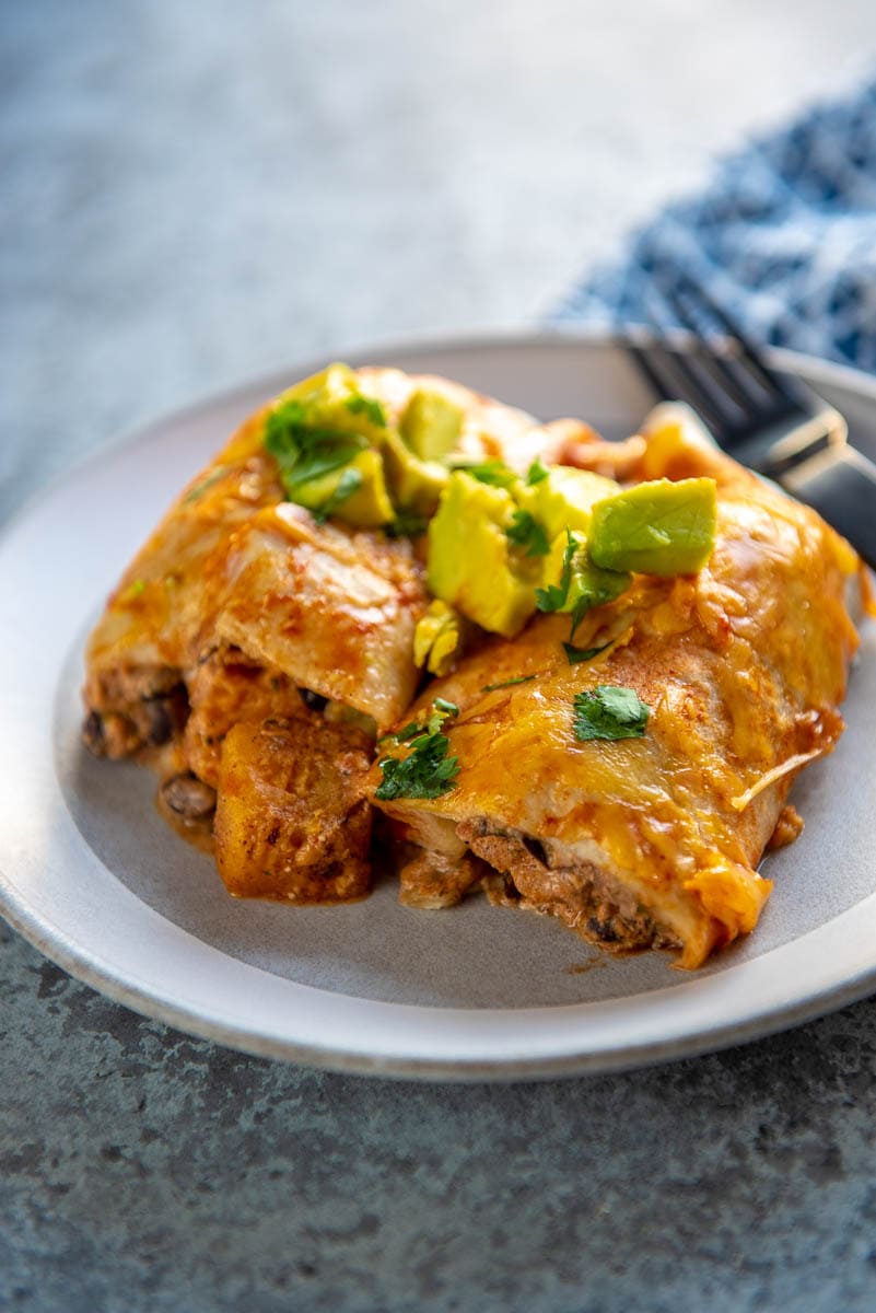 butternut squash enchiladas topped with avocado on a gray plate