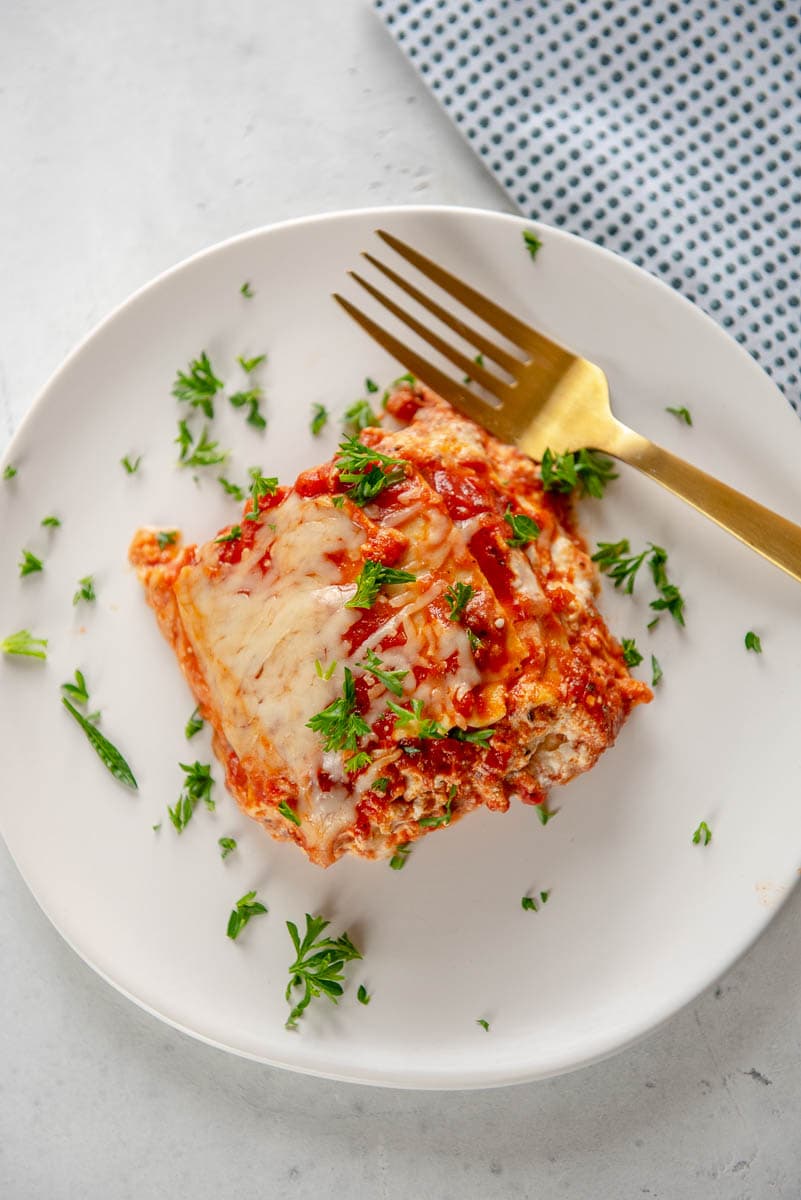 piece of lasagna on white plate with gold fork