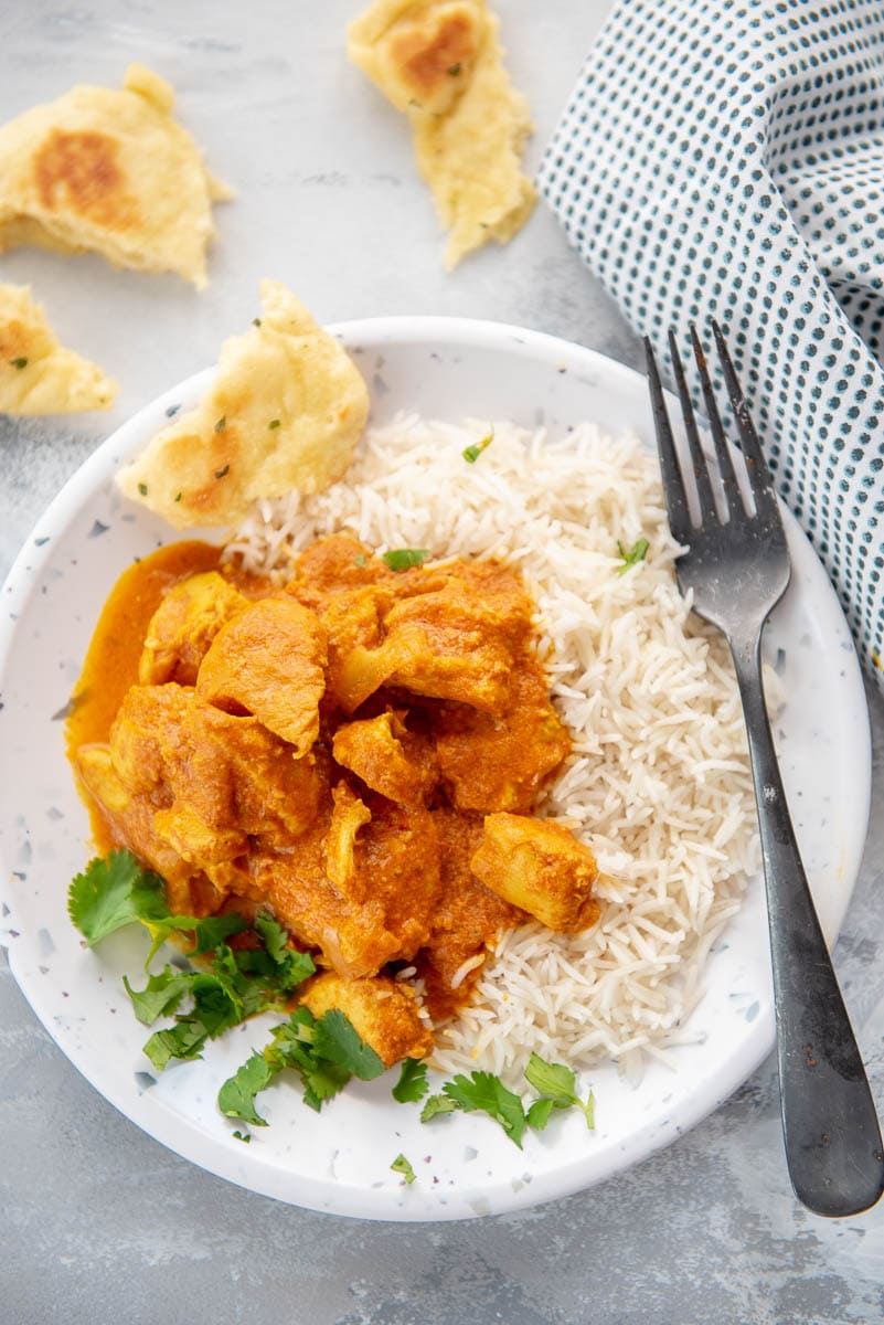 serving of butter chicken over rice with naan on white plate