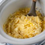 stirring mashed potatoes in slow cooker with spoon