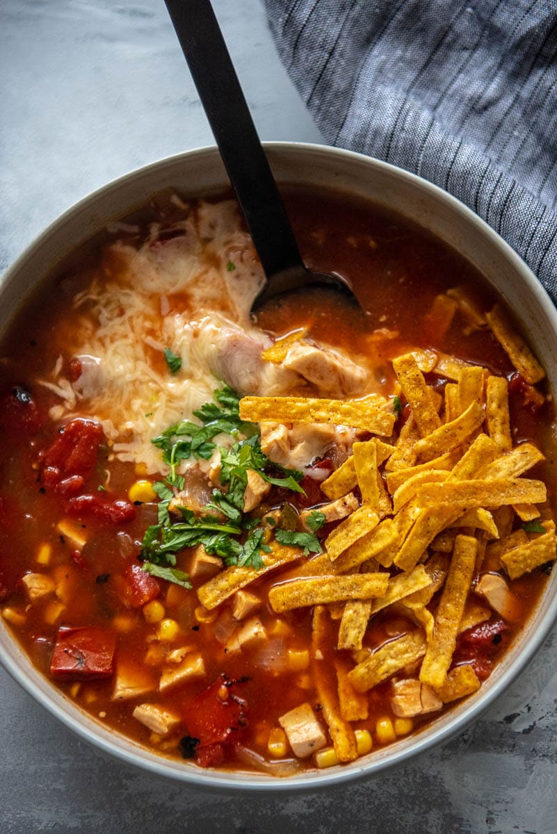 gray bowl of chicken tortilla soup topped with tortilla strips, melted cheese and cilantro