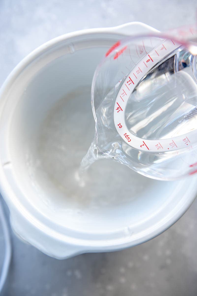 pouring measuring cup of water into slow cooker