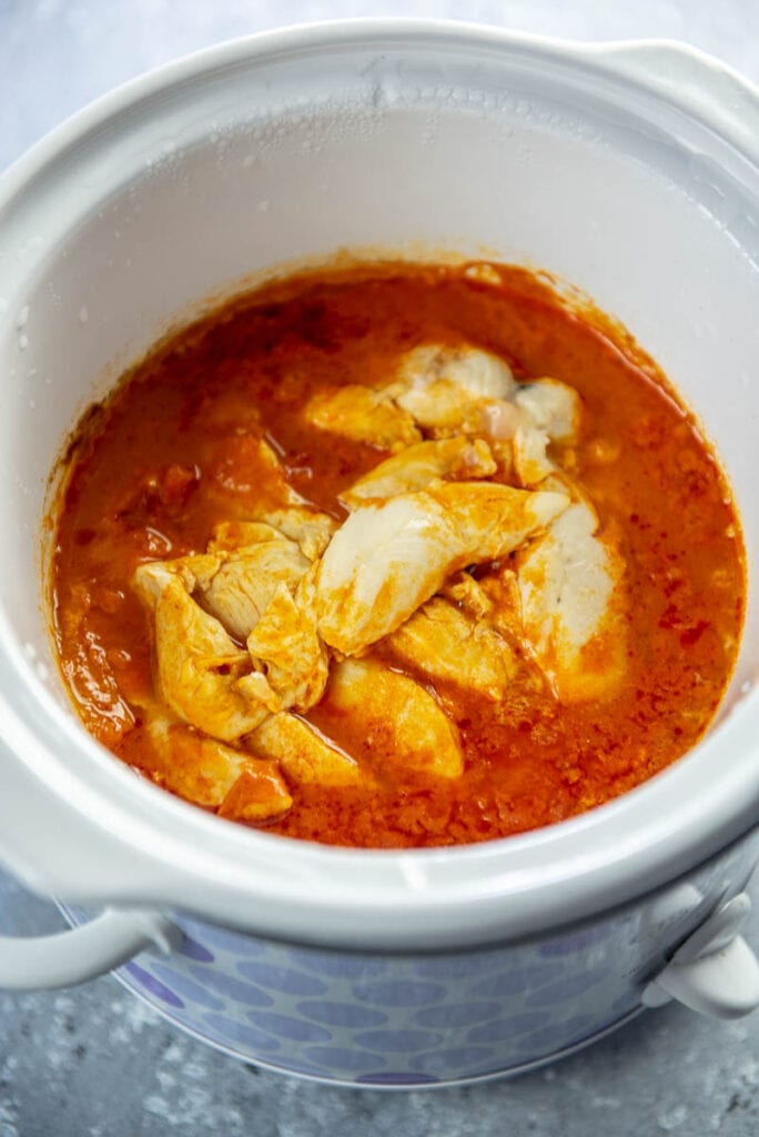 slow cooker with cooked chicken breasts and buffalo sauce