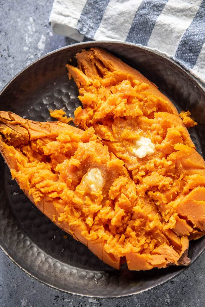 baked sweet potato cut open and topped with butter on plate