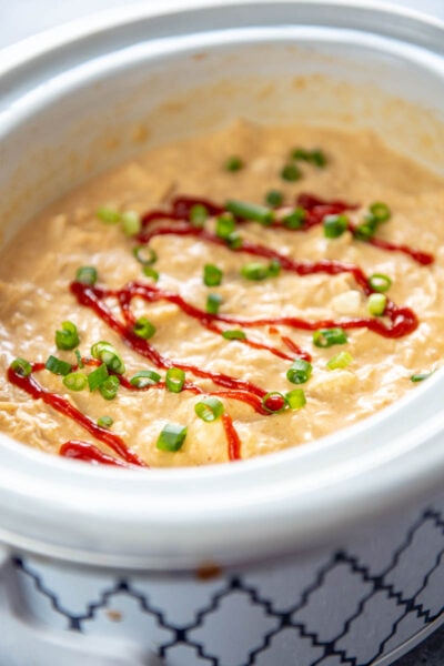slow cooker with dip topped with sriracha sauce and green onions