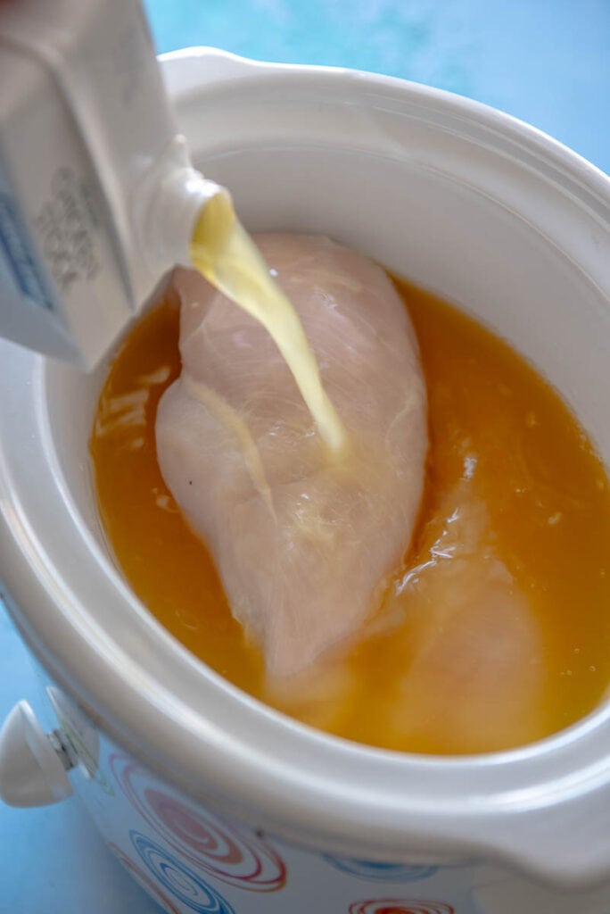adding broth to chicken breasts to cook in slow cooker