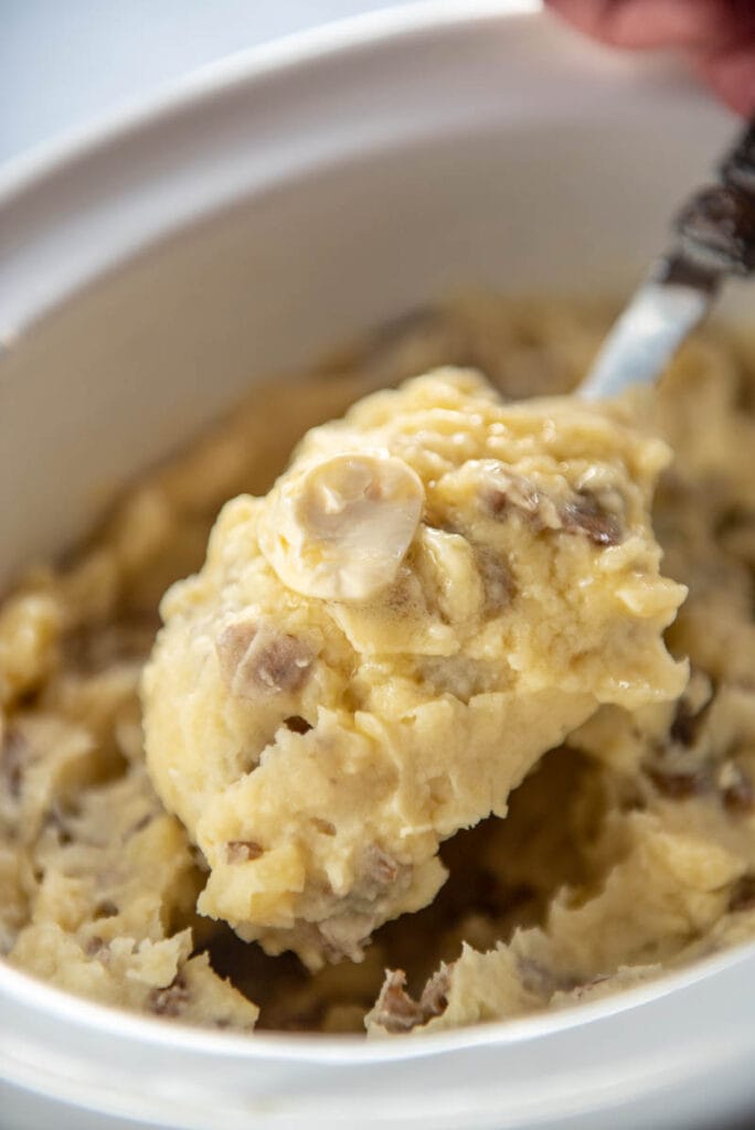 scooping a spoonful of mashed potatoes out of slow cooker