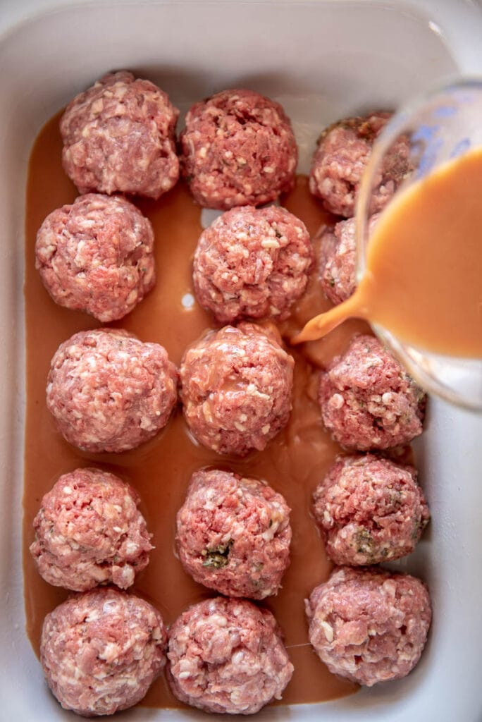 pouring sauce over uncooked meatballs in slow cooker