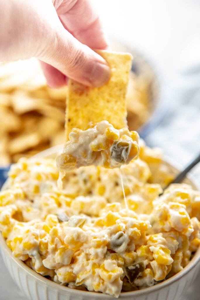 dipping chip into white bowl filled with corn dip
