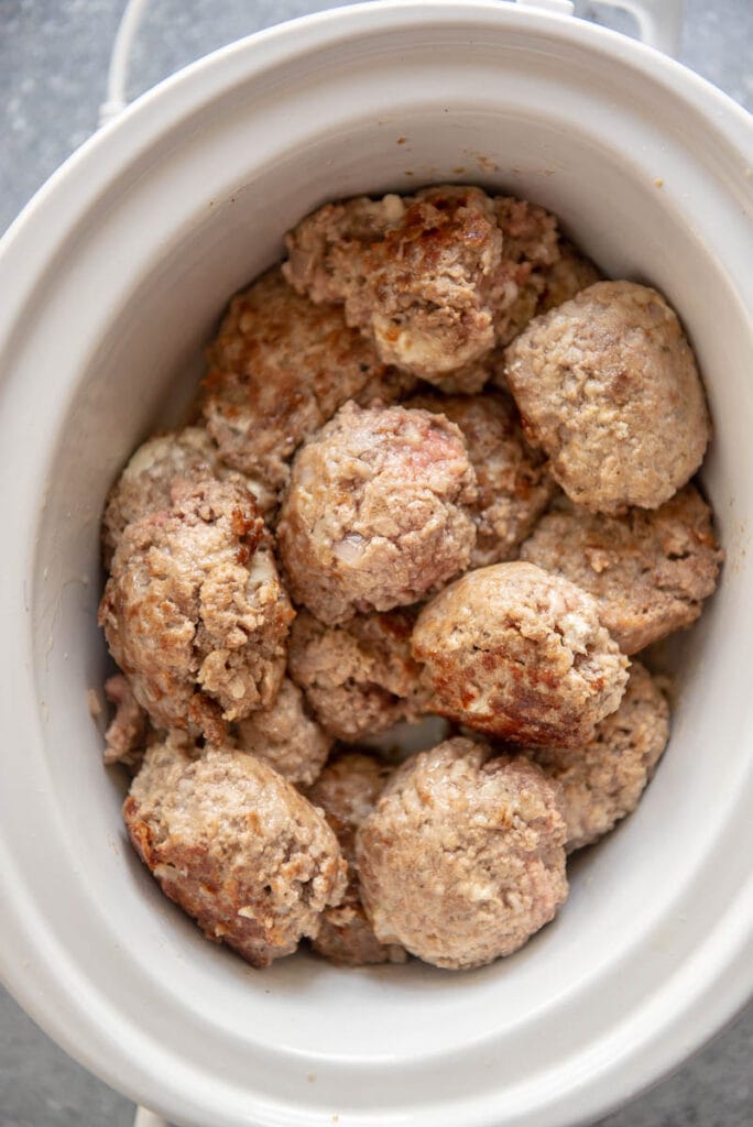 browned meatballs in oval white slow cooker ready to cook