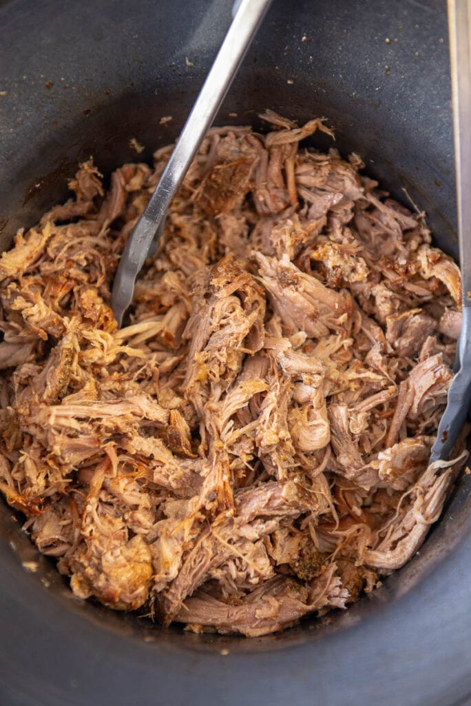 shredded pork with tongs in round slow cooker